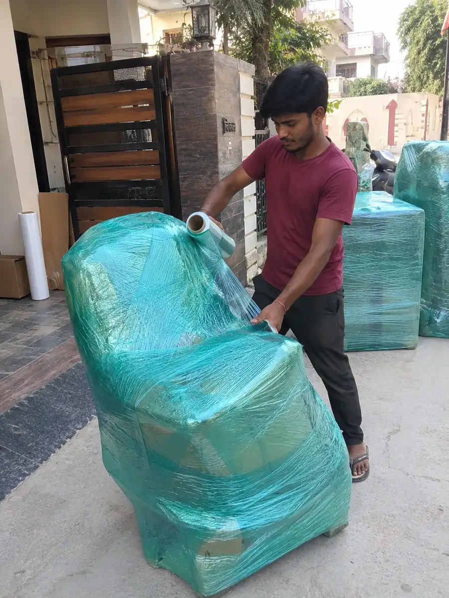 A mover wrapping a chair in corrugated sheet and stretch film in Dehradun